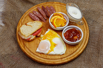 Natural homemade breakfast of scrambled eggs, toast, hunting sausages and jam, laid out on a wooden plate. The concept of healthy and tasty breakfast.