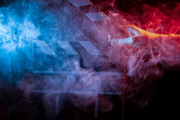 Black and white opened clapperboard for cinema close up among multicolored red and blue smoke in a man’s hand giving a command to start shooting on a black isolated background