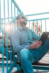 A middle-aged man uses a tablet device outdoors.A man enjoying music vibes through the headphones...