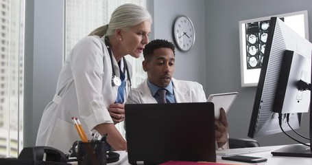 Millennial male doctor using tablet and looking at computer screen with colleague. Two medical doctors working inside office using technology