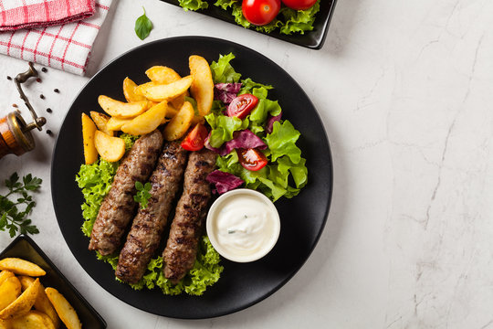 Traditional cevapcici served with baked potatoes. Flat lay. Stone background.