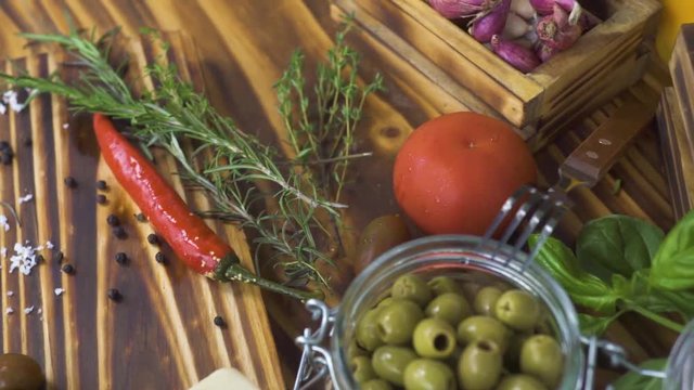 Close up vegetables pepper, tomato, onion, garlic and herbs rosemary, salt, olives for cooking food on kitchen. Trecking shot vegetables and seasoning herbs on wooden table.