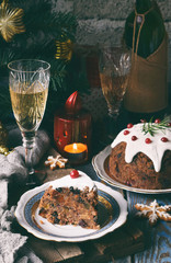 Traditional english Christmas steamed pudding with winter berries, dried fruits, nut in festive setting with Xmas tree and burning candle. Fruit cake.