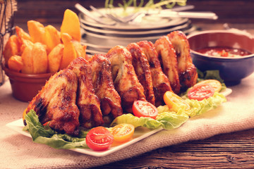 Roasted chicken wings with baked potato on the table, close up vintage view