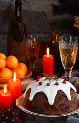 Traditional english Christmas steamed pudding with winter berries, dried fruits, nut in festive setting with Xmas tree and burning candle. Fruit cake.