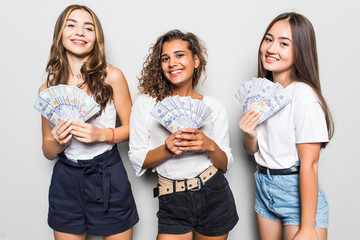 Portrait of multiethnic women expressing irritation while lucky female friend holding lots of money dollar cash isolated over gray background