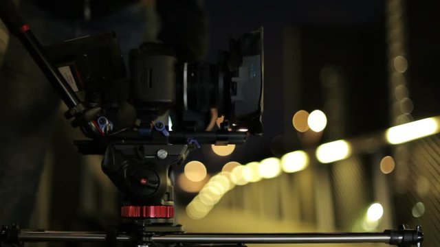 video dslr camera advancing on slider with lights and a fence in background. behind the scenes video production 