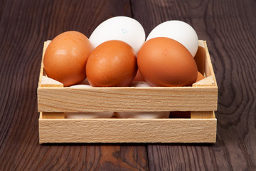 White and brown eggs in wooden crate on wooden background.