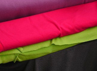 vertically stored wool fabric bales in the colours purple, pink, light green, dark grey, plenty of space for your own text, well suited as background in a picture