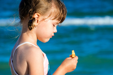 Little girl stands with her eyes down and holds one potato chip in her hand