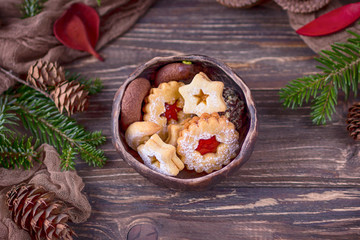 Homemade assorted Christmas cookies in ceramic bowl, christmas tree branch and pine cones on a wooden background