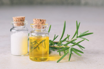 Rosemary essential oil in a small bottle and fresh twig on light background. Natural aroma cosmetic oil and salt