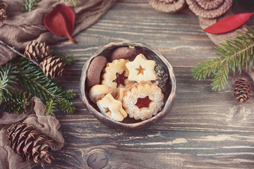 Christmas cookies in ceramic bowl, christmas tree branch and pine cones on a wooden background. Toned photo