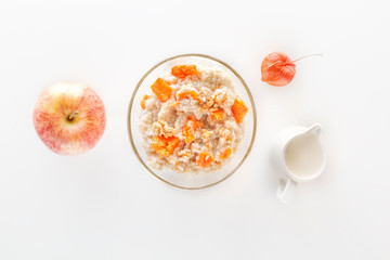 Oatmeal with pumpkin and nuts in a glass plate and a jug with milk on a white background. Top view