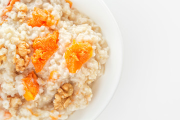 Oatmeal with pumpkin and nuts in a white plate on a white background. View from above. Copy space. Close-up