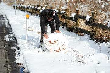Teenage boy playing with snow next to a wooden trunk fence. Shizuoka Prefecture, Japan. Winter of February 2011.