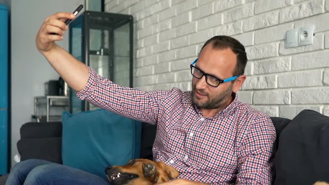 Young, happy man taking selfie with his dog on sofa at home