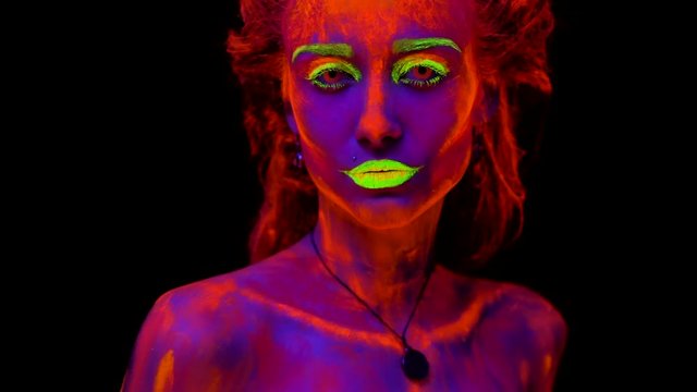 A beautiful young sexy half-naked girl dancing with glowing paint on her body in black light. Pretty woman with glowing bodyart in black lamp light.