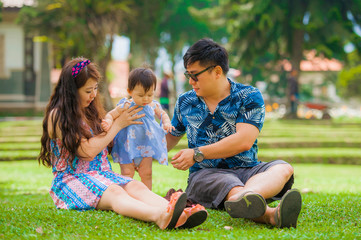 young happy loving Asian Japanese family with parents and sweet baby daughter at city park together with father taking selfie pic with mobile phone