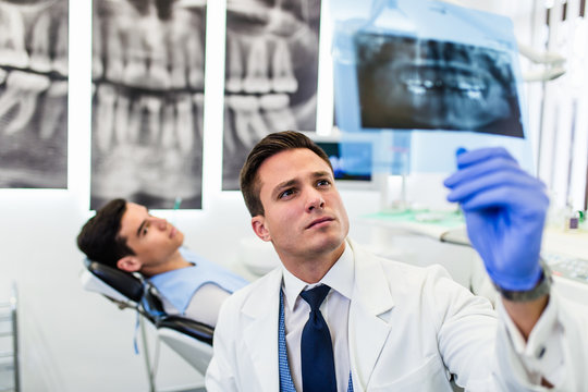 Portrait of handsome smiling dentist looking at x-ray image of his patient.