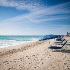 Fototapeta premium Open umbrellas on the sandy shore near the ocean. Beach in Miami, Florida. Empty beach. Seaside. Early morning. Clouds