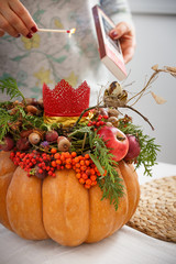 Closeup of hands of a young woman light a candle in an autumn pumpkin floral arrangement. Thanksgiving concept