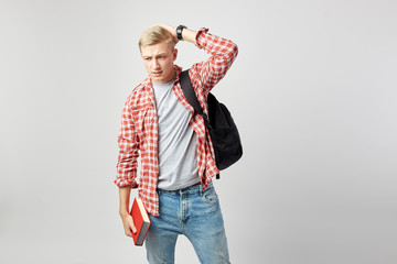 Blond guy with black backpack on his shoulder dressed in a white t-shirt, red checkered shirt and...