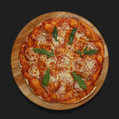 Appetizing pizza on a wooden board on a dark background. Classic feed.