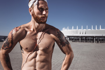 Relaxing after training on workout ground outdoors. Handsome shirtless sportsman looking away with...