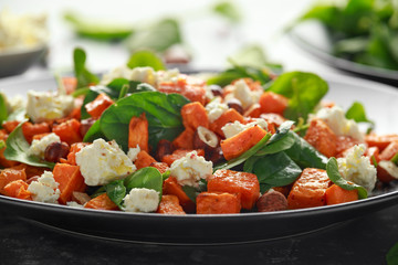 Healthy roasted sweet potato salad with spinach, feta cheese, hazelnut nuts in black plate