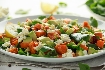 Avocado, roasted sweet potato, spinach, feta cheese healthy salad in white plate.