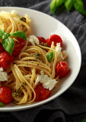 Pasta with green pesto sauce, roasted cherry tomatoes and mozzarella cheese in white plate on dark rustic background