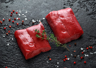 Raw venison steak with rosemary and pepper on black rustic table. - obrazy, fototapety, plakaty
