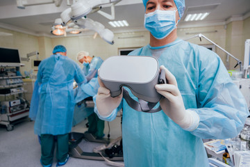 Doctor in a surgical room with virtual reality glasses on the background of the real operation.