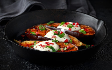 Grilled eggplants with yogurt sauce, pomegranate seeds, parsley and green onion in cast iron vintage pan.