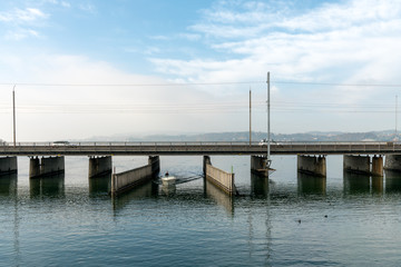 Fototapeta premium Rapperswil, SG / Switzerland - November 5, 2018: motorboat with female captain passes from the lower to the upper Lake Zurich through the passage on the Seedamm bridge near Rapperswil