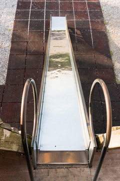 metal playground slide goig down onto a red mat ground in an outdoor playground