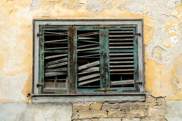 Fototapeta na wymiar horizontal view of old broken window shutters on a dilapidated and run down house front with chipped paint and plaster