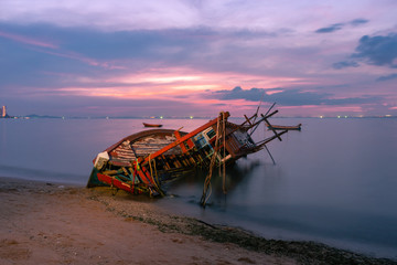 Fototapeta na wymiar Old fishing boat shipwrecks disposed on the beaches of the eastern coast of Thailand, view and landscape of the sea on sunset and sand with cloud sky.