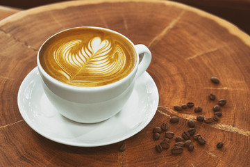 Cappuccino coffee in a white cup on a wooden table with a modern coffeeshop in the background and beas selective focus.