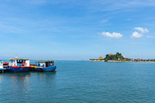 The view of the small island in the distance with the sea and the clear sky with fog with red fishing boat sailing in the ocean.