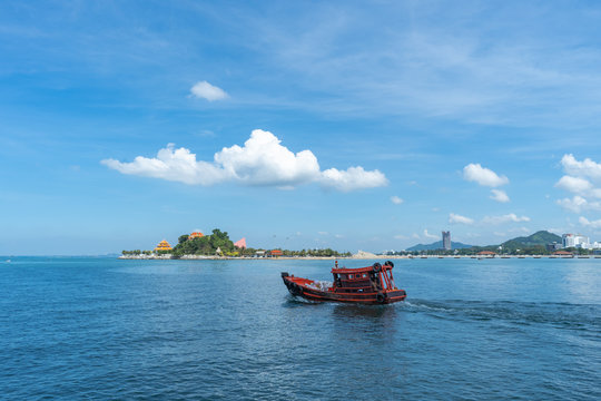 The view of the small island in the distance with the sea and the clear sky with fog with red fishing boat sailing in the ocean.