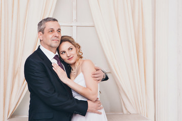 Wedding couple on the nature is hugging each other. Beautiful model girl in white dress. Man in suit. Beauty bride with groom. Female and male portrait. Woman with lace veil. Lady and guy outdoors