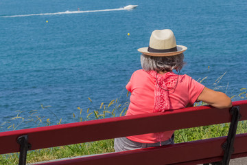 Obraz premium Femme au chapeau assise sur banc face à la mer