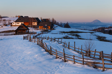 Spectacular winter landscape. Winter sunset, old rural mountain wooden chalets and snowy hills near Brasov, Transylvania, Romania, Europe