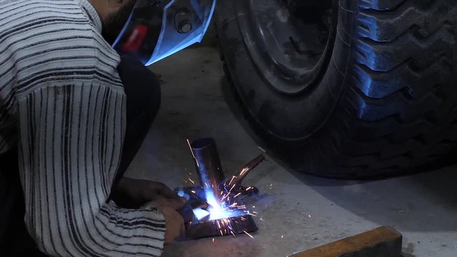 welder in protective mask connects metal parts using electric welding. red sparks fly to sides