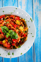Pasta with meat, tomato sauce and vegetables on wooden table