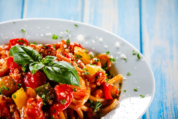 Pasta with meat, tomato sauce and vegetables on wooden table