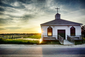 small white wooden chapel on the water on the coast during a colorful summer sunset with...