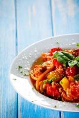 Pasta with meat, tomato sauce and vegetables on wooden table
